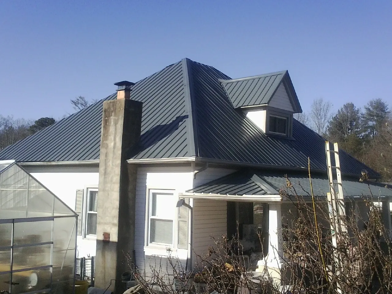Dark blue standing seam metal roof on a white farmhouse with dormer — Slate & Tile Roof Repair by Roofing Brothers in Soda Springs