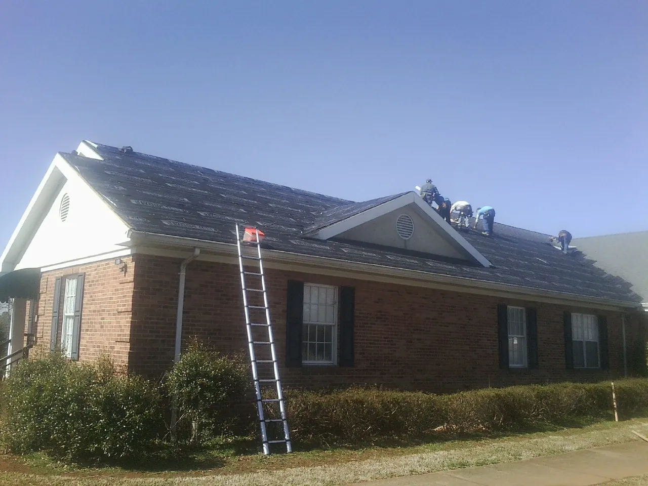Crew tearing shingles off a brick ranch roof with a ladder set — Metal Roof Repair work by our crew in Soda Springs