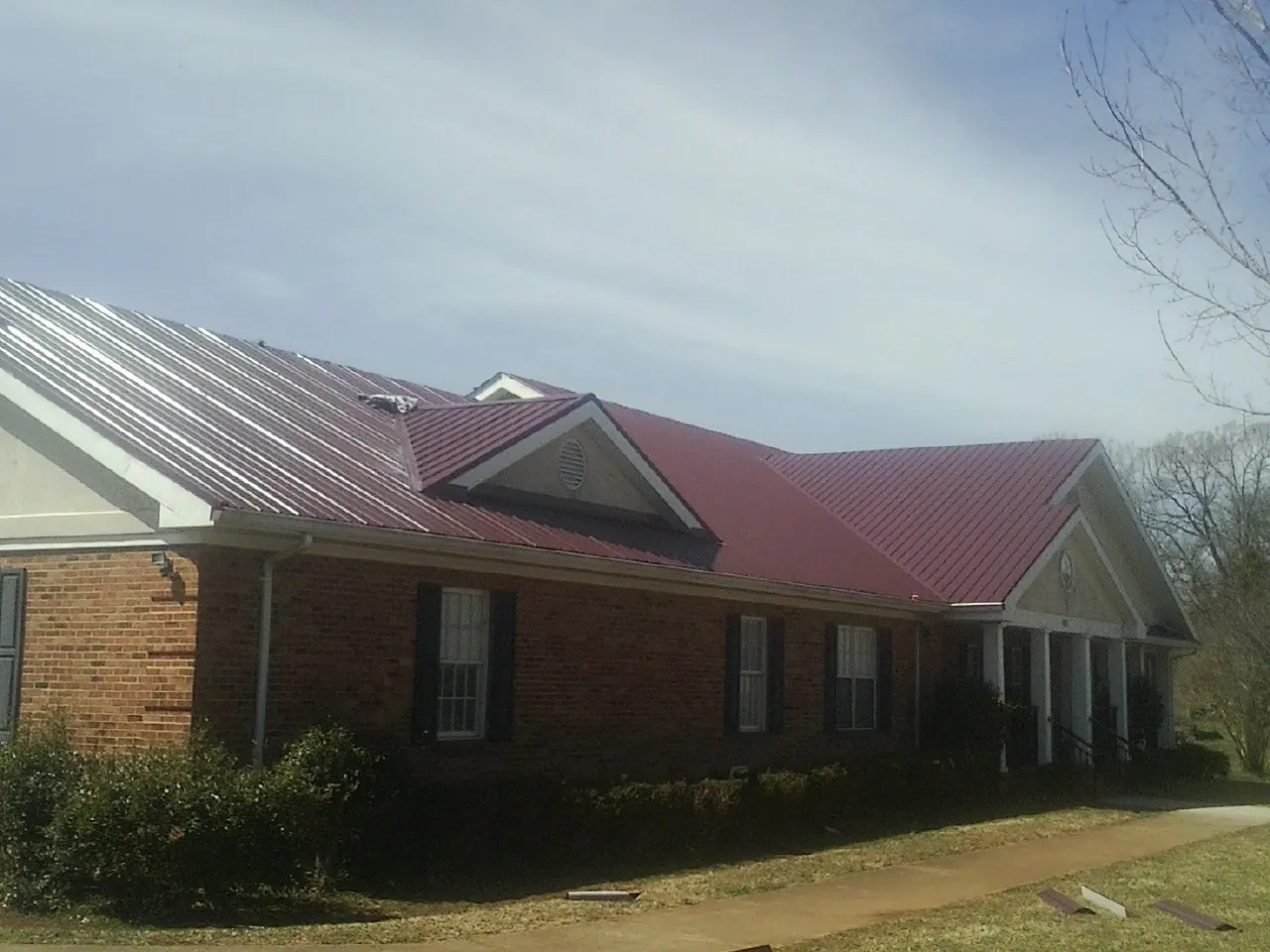 Red metal roof with gabled entries on a long brick building, from a Hail Damage Roof Repair job in Soda Springs