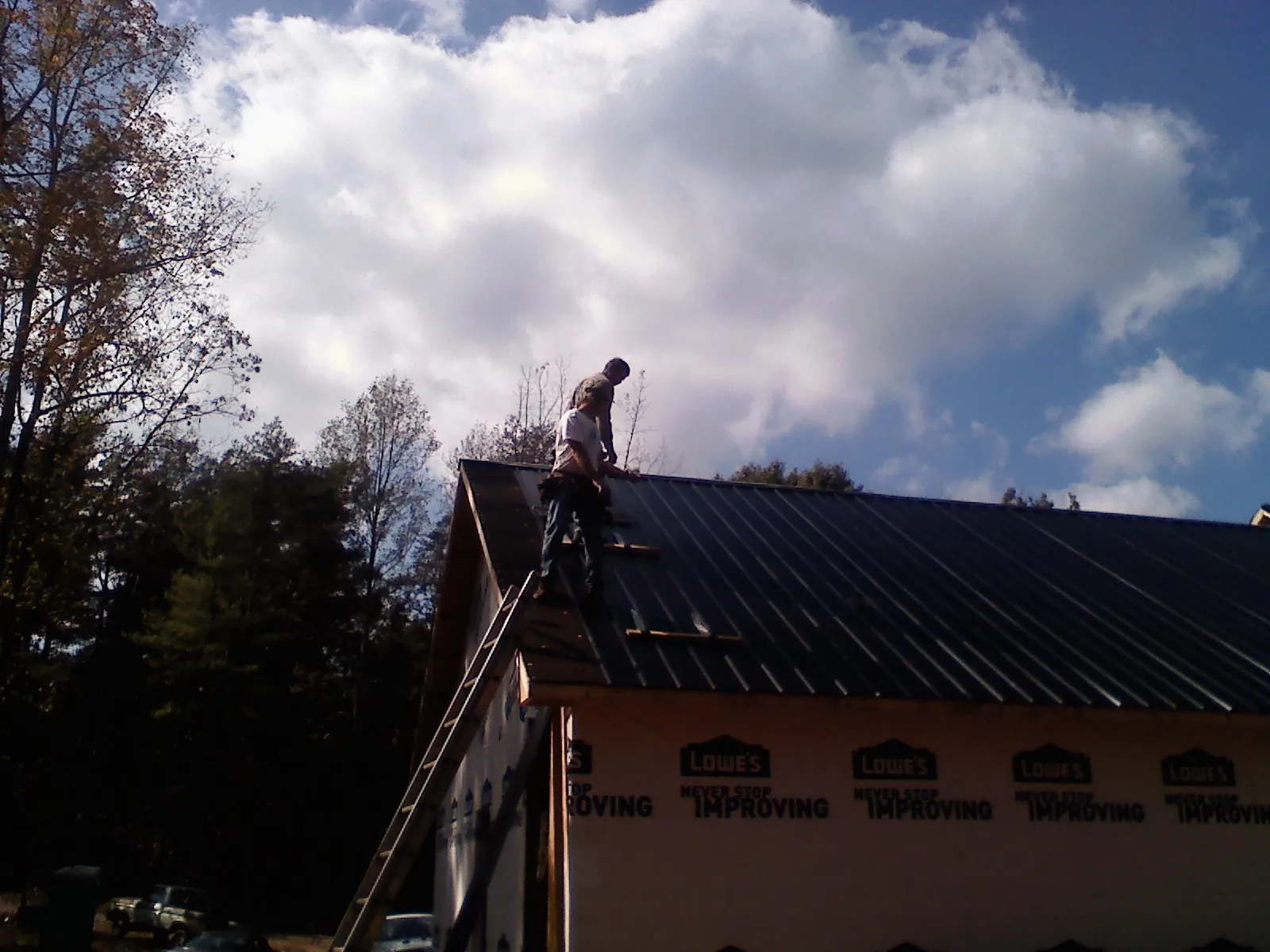 Roofer fastening dark metal panels high against a cloudy sky, from a Roof Inspection job in Soda Springs