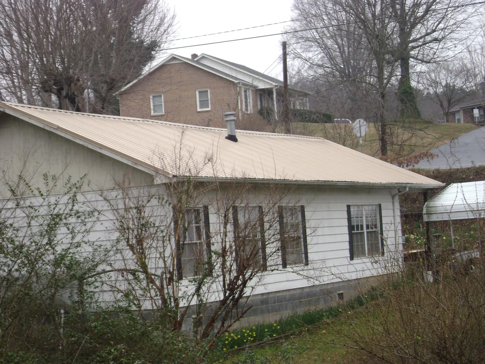 Tan metal roof on a white sided house set into a hillside — Commercial Roofing by Roofing Brothers in Soda Springs